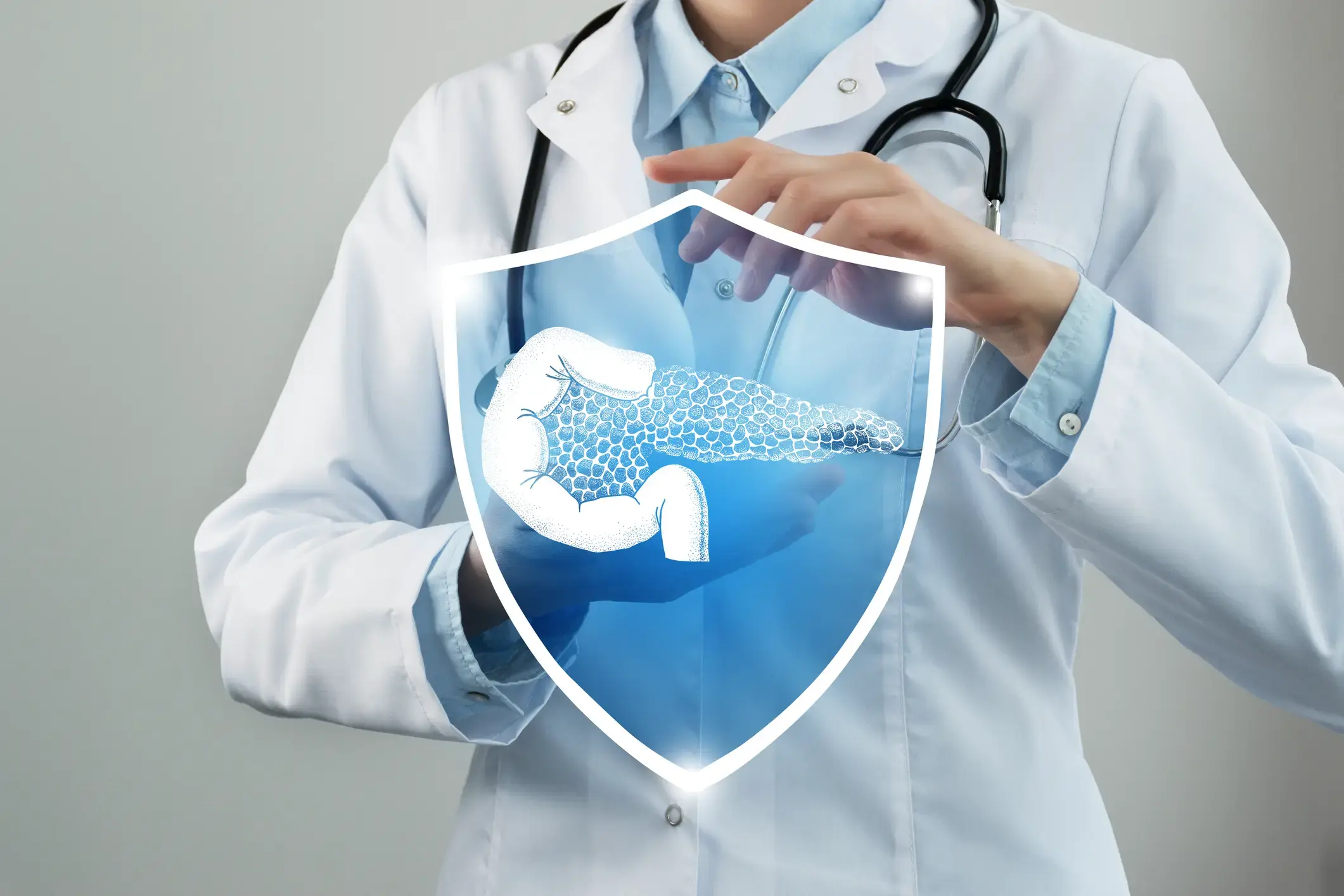 Eine medizinische Fachkraft steht vor grauem Hintergrund, während vor ihr, im Vordergrund ein blaues Schild projiziert ist. Im projizierten Schild ist in Weiß ein Pankreas abgebildet und in Form von Kreisen, Insulin-produzierende Betazellen, neben dem Pankreas, ist ein Zwölffingerdarm, auch in Weiß, abgebildet. 