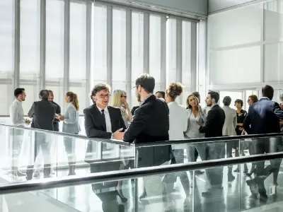 Eine Gruppe von Fachleuten in formeller Kleidung beim Networking in einem modernen Büroraum mit Glaswänden. 