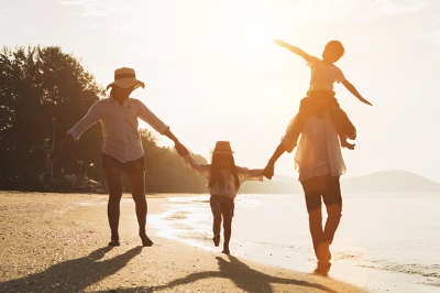 Famille de quatre personnes marchant main dans la main sur une plage au coucher du soleil, montagnes en arrière-plan