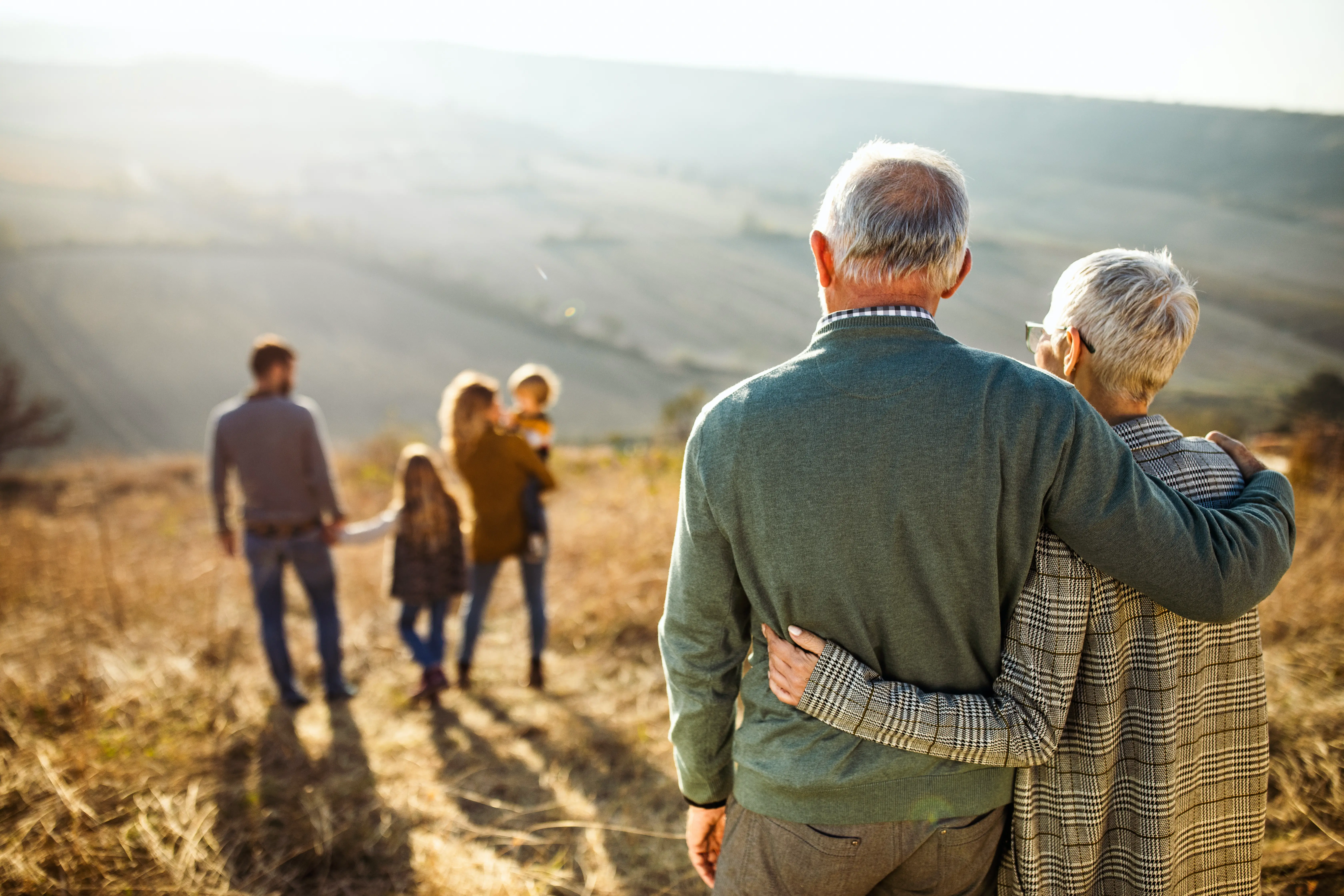 Drei Generationen einer Familie, die gemeinsam bei Sonnenuntergang durch ein Feld spazieren