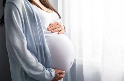 Une future maman debout, les mains posées sur son ventre arrondi.